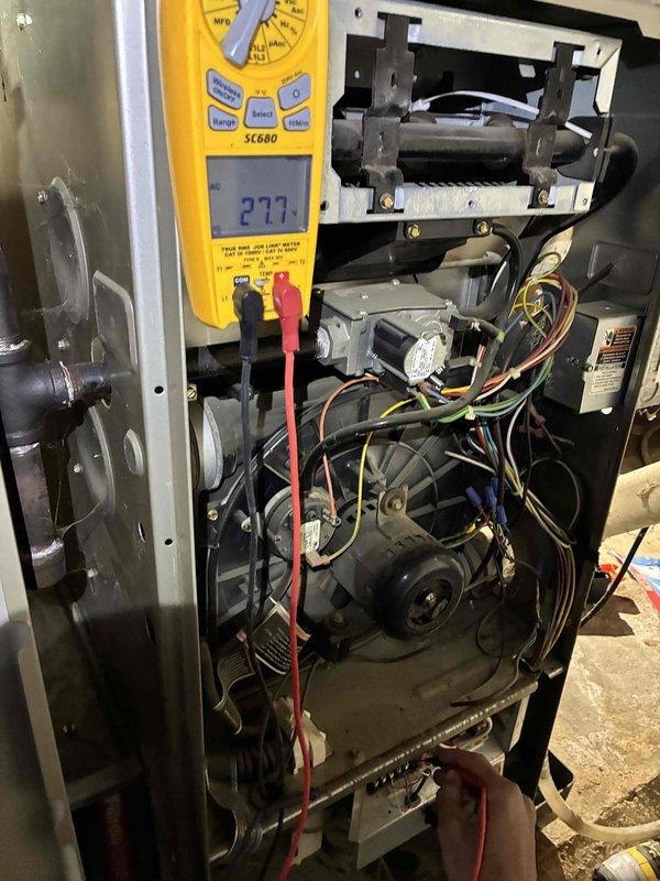 Diagnosed high CO levels (702 ppm/863 ppm AF) during combustion analysis with Testo 310, indicating incomplete combustion despite high efficiency (97.6%). Voltage testing with SC680 multimeter revealed 27.7V at control board, confirming proper voltage to components. Cleaned burner assembly and adjusted gas/air mixture to restore proper combustion parameters and eliminate the no-heat condition.