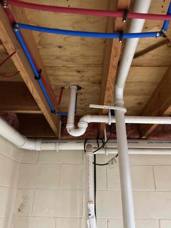 Completed installation of a PEX plumbing system in unfinished basement ceiling, including properly secured hot and cold water lines with brass valve fittings and white PVC drainage components. All pipes were properly mounted to wooden joists with appropriate brackets, ensuring a code-compliant installation with no leaks observed during final inspection.