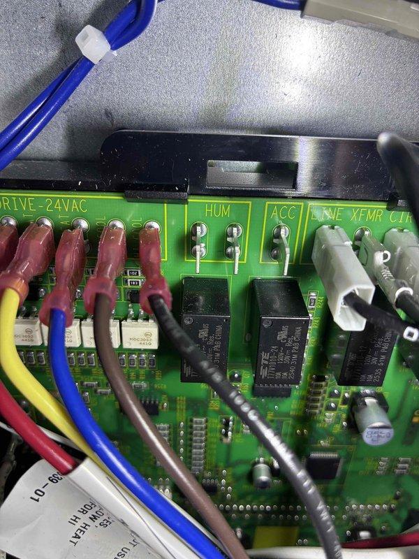 Performed diagnostic inspection of control board in HVAC system following installation callback. Inspected terminal connections and wiring configuration on the main circuit board, focusing on the relay components and 24VAC control circuit. Verified proper wire terminations at DRIVE-24VAC, HUM, ACC, and LINE XFMR CTR connection points to ensure proper system operation.