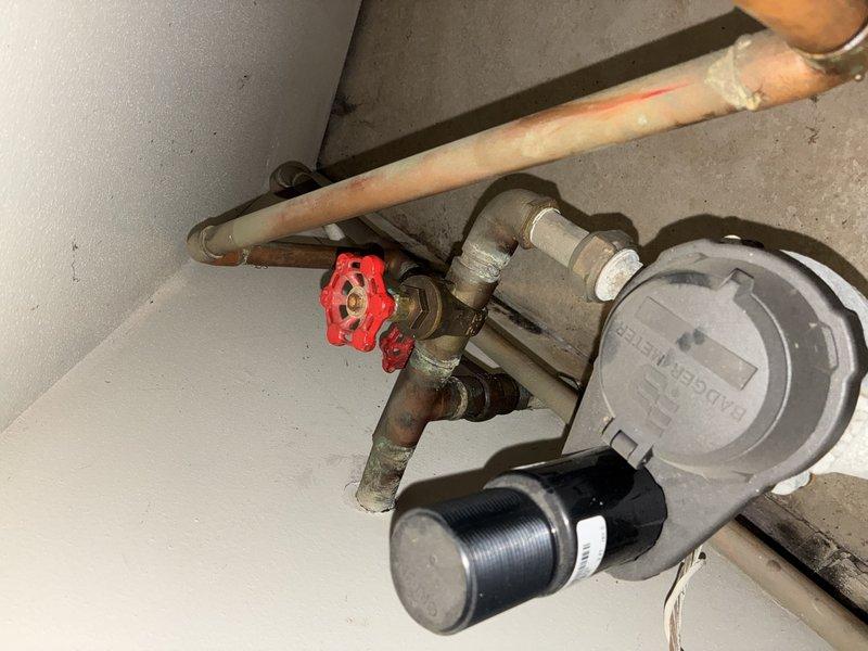 Conducted inspection of an aging water heater installation with significant copper pipe oxidation and mineral buildup at connection points. Documented existing plumbing configuration including copper/PVC pipe integration, valve assembly with prominent red handle, and pressure regulator system. Noted several areas requiring attention including corrosion at pipe junctions, deteriorating insulation, and potential flow restriction due to mineral deposits.