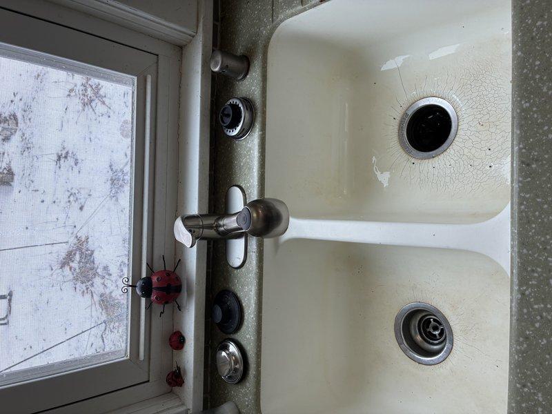 Inspected kitchen sink with dual basin and found ceramic material cracking around drain opening. Evaluated plumbing connections including copper supply lines, PVC fittings, and braided flexible hoses which were properly secured with mounting brackets. Replaced damaged faucet assembly and verified proper operation with no leaks.