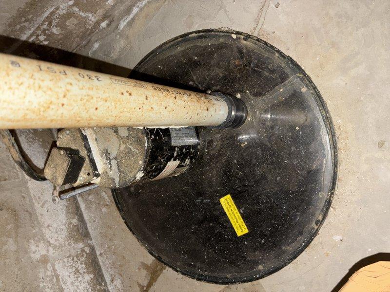 Conducted inspection of existing sump pump system in basement, documenting significant moisture intrusion and staining on cinder block foundation walls. Observed aging sump basin with visible sediment accumulation and corrosion on discharge piping. Recommended replacement of complete system including new basin, pump, check valve, and PVC discharge piping to prevent potential basement flooding.