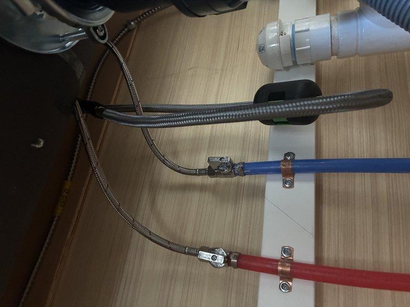 Installed new matte black kitchen faucet with pull-down sprayer head on granite/quartz countertop, connecting to existing supply lines. Secured all braided metal flexible hoses with proper metal clamps and verified connections to the blue cold water and red hot water supply pipes. System tested with no leaks observed.