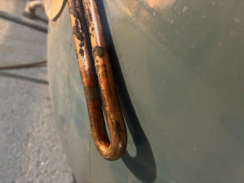Inspected water heater system and documented significant copper heating element deterioration. Element exhibited advanced corrosion with extensive reddish-brown oxidation throughout, particularly severe at the U-bend section. Photographic documentation was taken to show condition of component requiring replacement due to compromised integrity.