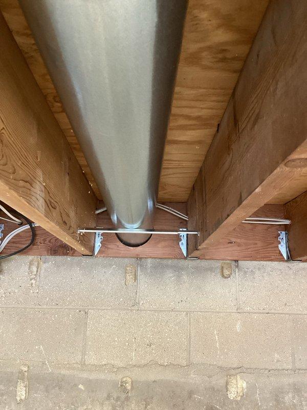 Installed cylindrical galvanized steel ductwork in basement/crawlspace area, securing the main trunk line to wooden joists with proper metal brackets and supports. The ductwork was successfully integrated with the existing infrastructure, running horizontally across the ceiling structure with connections to the ventilation system through the concrete block wall.