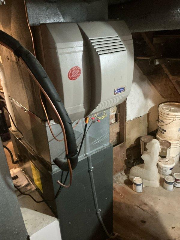 Performed inspection of existing Carrier furnace system with integrated humidifier in basement utility area. Documented current installation conditions including electrical connections, ductwork configuration, and adjacent plumbing infrastructure. Evaluated replacement options based on observed brick wall construction, existing vertical pipe runs, and available utility connections for optimal new system placement.
