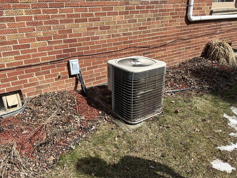# HVAC System Replacement Estimate

Conducted comprehensive evaluation of existing residential HVAC system for replacement. Assessed indoor air handler unit with current 14x25x1 filtration system and connected ductwork infrastructure. Documented furnace cabinet access panel with operational instructions and existing insulated supply plenum connections. Evaluated electrical wiring configuration and mounting hardware for indoor equipment.

Inspected outdoor condensing unit positioned on concrete pad against brick exterior wall. Unit exhibits cylindrical design with horizontal fin configuration typical of older model air conditioners. Documented electrical disconnect box mounted to structure with conduit routing to outdoor unit. Assessed concrete pad condition showing weathering and vegetation growth, indicating extended service life. Noted landscape mulch bed proximity to equipment and drainage considerations for replacement installation.

Prepared equipment specifications and replacemen
