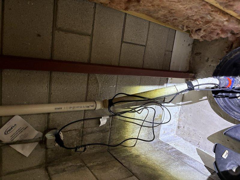 # Plumbing Estimate - Sump Pump

Conducted comprehensive assessment of existing sump pump system in basement crawl space. Inspected sump basin installation, pump mechanism, and associated discharge piping configuration. Evaluated PVC discharge line connections, check valve installation, and electrical cord routing for code compliance and operational efficiency. Documented current pump positioning within basin and verified proper float switch clearance. Assessed surrounding concrete floor conditions and structural framing around pit opening. Noted deteriorated fiberglass insulation in overhead joist bays indicating potential moisture infiltration concerns that may impact pump workload. Photographed complete system layout including piping connections, basin condition, and utility area infrastructure to provide detailed documentation for estimate preparation.
