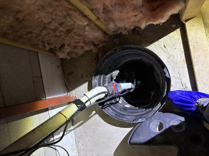 # Plumbing Estimate - Sump Pump

Conducted comprehensive assessment of existing sump pump system in basement crawl space. Inspected sump basin installation, pump mechanism, and associated discharge piping configuration. Evaluated PVC discharge line connections, check valve installation, and electrical cord routing for code compliance and operational efficiency. Documented current pump positioning within basin and verified proper float switch clearance. Assessed surrounding concrete floor conditions and structural framing around pit opening. Noted deteriorated fiberglass insulation in overhead joist bays indicating potential moisture infiltration concerns that may impact pump workload. Photographed complete system layout including piping connections, basin condition, and utility area infrastructure to provide detailed documentation for estimate preparation.