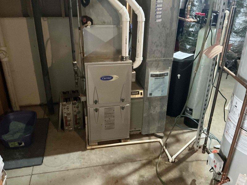 # HVAC System Estimate - Equipment Replacement

Conducted comprehensive evaluation of existing residential HVAC system for replacement estimate. Assessed current Carrier brand forced-air furnace installation located in basement mechanical room, including examination of white PVC venting configuration, refrigerant line routing, and electrical service connections. Documented existing equipment specifications and installation conditions including concrete block foundation walls, exposed structural framing, and utility room layout constraints.

Evaluated exterior Carrier condensing unit positioned against home's foundation, noting current mounting location, electrical disconnect placement, and refrigerant line penetrations through exterior wall. Assessed site conditions including ground-level installation pad, clearance requirements, and existing PVC conduit routing. Examined condition of outdoor unit including cabinet integrity, coil accessibility, and fan grille protection.

Documented m