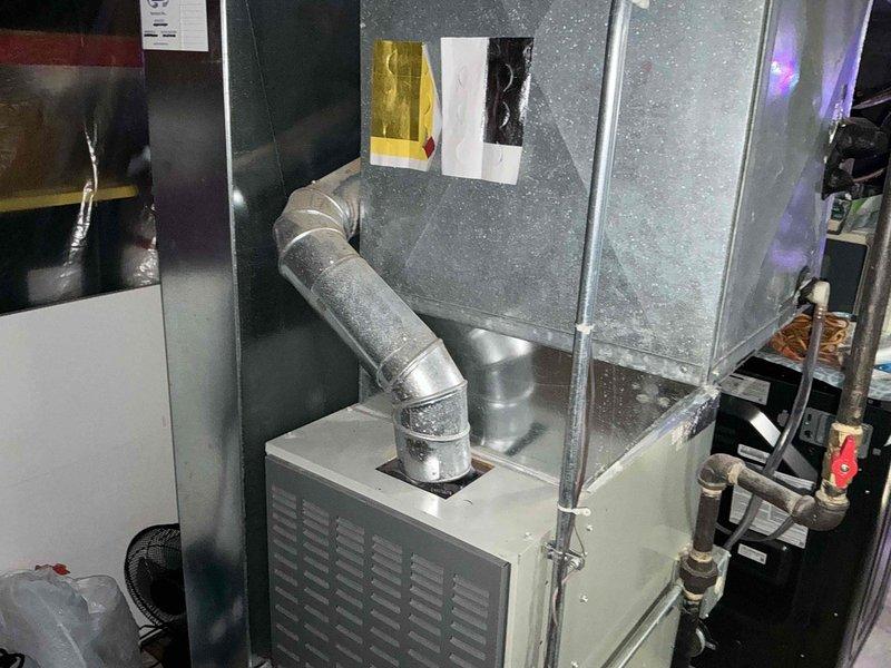 Completed full HVAC system replacement in basement utility area, installing new gray metal air handler unit with integrated ductwork connections and flexible supply duct routing. The installation included proper mounting of the heating/cooling equipment, connection of refrigerant lines, and integration with existing ductwork infrastructure, with all components secured and operational in the mechanical space.
