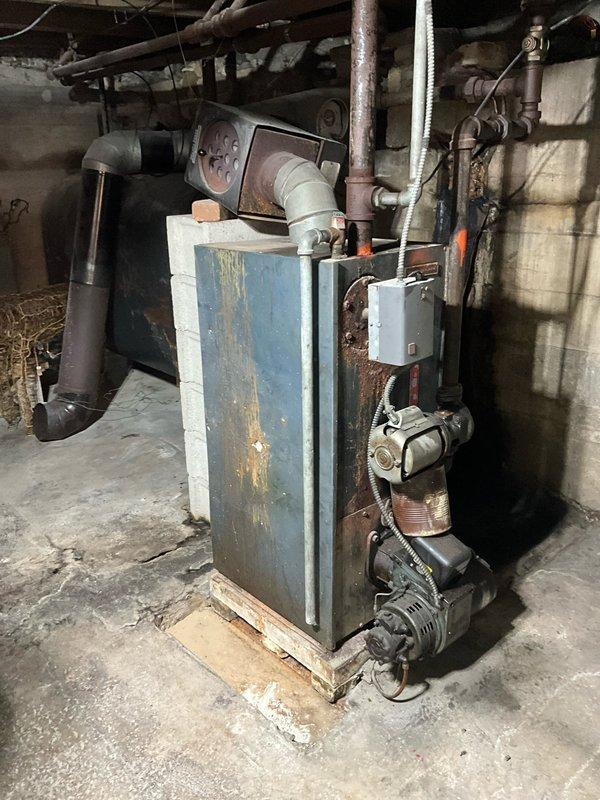 Completed comprehensive HVAC estimate for complete heating system replacement in residential basement. Existing equipment consists of an aging furnace with significant deterioration, including extensive rust on the blue-painted cabinet exterior, corroded panels, and paint failure indicating prolonged moisture exposure and end-of-service-life condition. The current installation includes a deteriorated boiler unit with associated pumping equipment, various aging piping configurations including metal and PVC connections, and outdated ductwork systems. Assessed all mechanical components, electrical connections, venting arrangements, and spatial requirements for new equipment installation. Documented existing system layout including cinder block enclosure, ceiling-mounted ductwork, exposed joists, and concrete floor conditions to determine optimal replacement configuration and any necessary structural modifications for modern high-efficiency equipment installation.