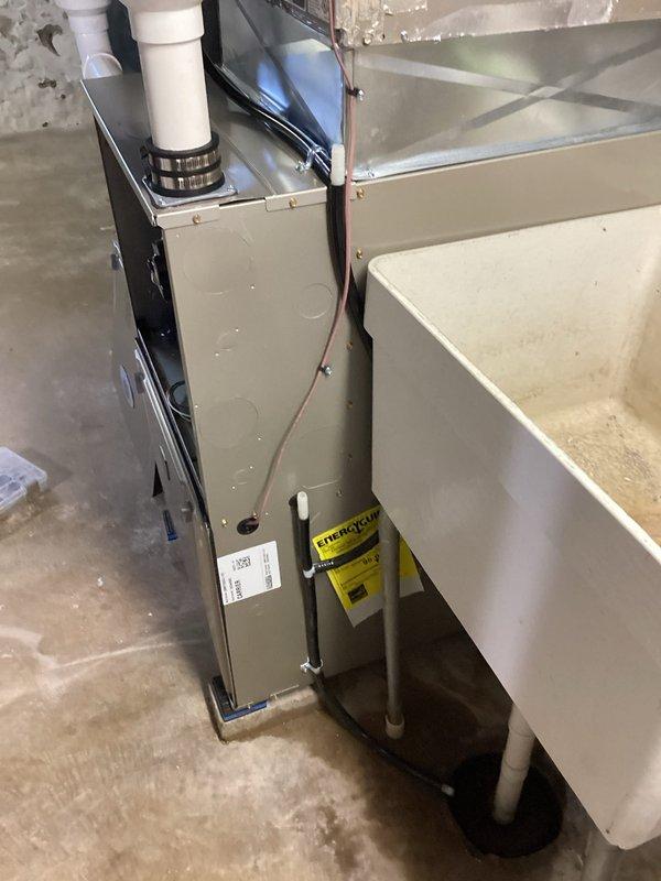 Completed HVAC system installation in residential basement utility area. Installed new beige cabinet furnace unit with dual white PVC intake and exhaust venting pipes routed vertically through ceiling structure. Configured sheet metal ductwork with angular transitions to integrate with existing air distribution system. Positioned white condensate pump adjacent to furnace on concrete floor for proper drainage management. Secured all metallic ductwork connections along ceiling joists with appropriate hangers and supports. Verified proper clearances from concrete block walls and ensured all venting, electrical connections, and drainage components meet manufacturer specifications and local code requirements. System tested and operational upon completion of installation warranty work.