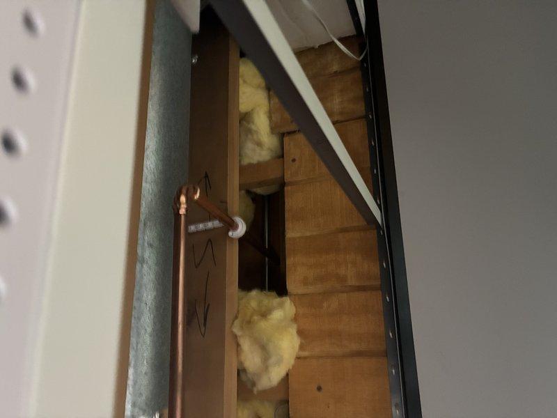 Responded to service callback to inspect and address plumbing concerns in deteriorated upper-level structure. Upon arrival, discovered exposed copper supply line running vertically through compromised ceiling area with significant structural deterioration, including extensive paint failure, water damage, and charred surfaces indicating previous fire damage. Accessed attic space through ceiling opening to evaluate copper piping installation and verify proper support and insulation clearances around pipe penetrations through floor joists. Confirmed copper line routing and connections were secure despite surrounding structural compromise. Documented existing conditions showing fiberglass insulation placement around framing members and pipe penetrations for reference.