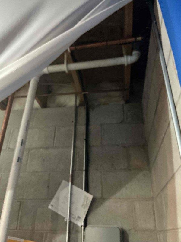 Performed comprehensive plumbing assessment for water heater replacement, including evaluation of existing infrastructure and drainage systems. Inspected overhead plumbing access point revealing multiple water supply lines and PVC drainage pipes running through ceiling joists, confirming adequate routing for new water heater connections. Examined basement sump pump system with vertical discharge piping to verify proper drainage capacity and ensure compatibility with water heater installation requirements.
