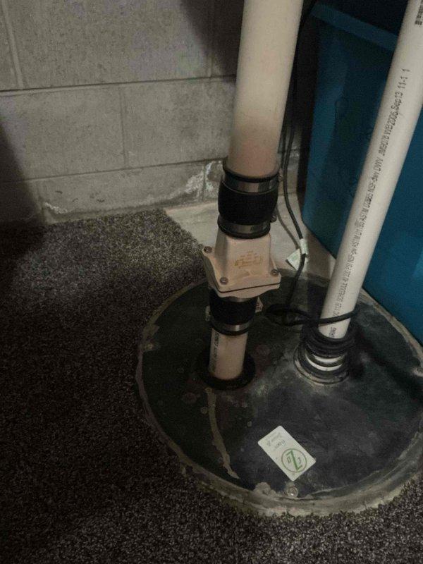 Performed comprehensive plumbing assessment for water heater replacement, including evaluation of existing infrastructure and drainage systems. Inspected overhead plumbing access point revealing multiple water supply lines and PVC drainage pipes running through ceiling joists, confirming adequate routing for new water heater connections. Examined basement sump pump system with vertical discharge piping to verify proper drainage capacity and ensure compatibility with water heater installation requirements.