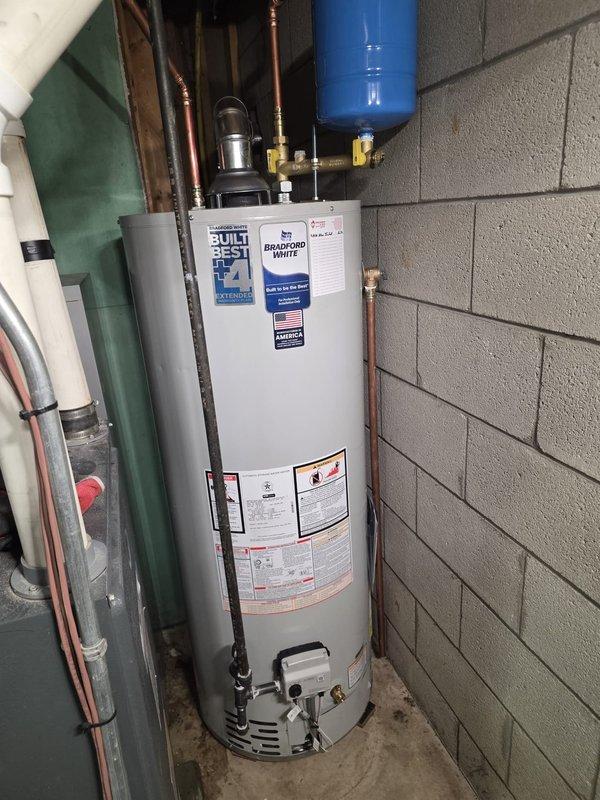 Completed installation of Bradford White RM250S6N residential water heater with 50-gallon capacity and 40,000 BTU/hr natural gas input in basement utility room. Installed blue expansion tank with proper brass fittings and copper piping connections, ensuring all plumbing connections meet manufacturer specifications and local code requirements. Verified proper clearances, tested system operation, and confirmed all safety labels and operational specifications are visible and intact per ANSI Z21.10.1-2013/CSA 4.1-2019 standards.
