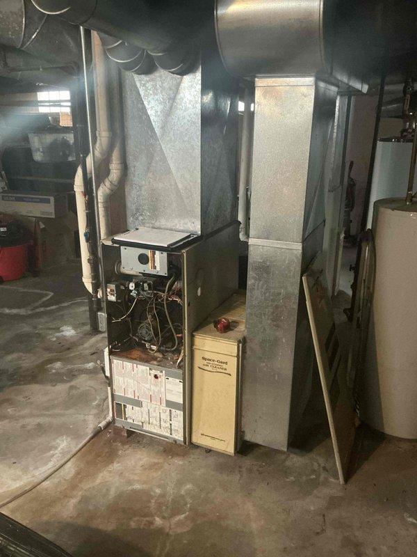 Completed comprehensive HVAC system evaluation for furnace replacement in residential basement mechanical room. Assessed existing furnace unit with exposed internal components including blower motor assembly, evaluated connected galvanized ductwork and plenum configuration, and inspected attic structural framing to determine accessibility and routing requirements for new system installation.