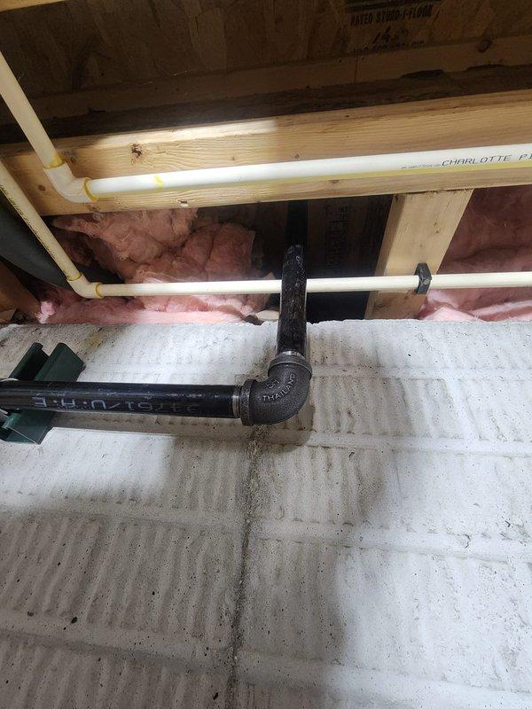 Installed hanging heater unit in basement area with exposed floor joists and existing utility infrastructure. Positioned and mounted heater to accommodate multiple existing plumbing lines including PVC drainage pipes, black waste lines, and gray flexible ductwork while maintaining proper clearances from wooden structural members and insulation. Secured unit with appropriate mounting hardware to ensure stable installation in unfinished below-grade space with concrete foundation.