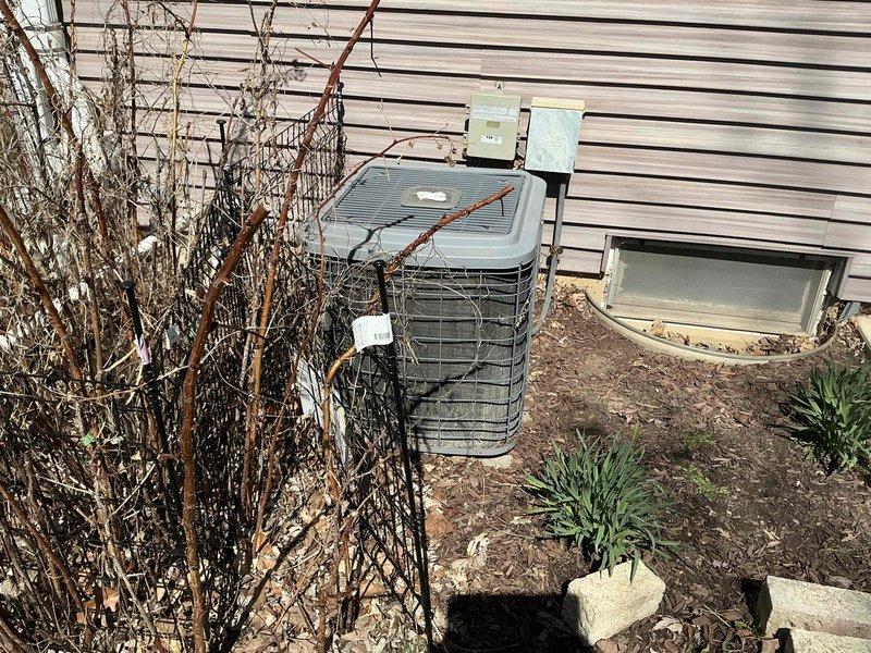 Conducted comprehensive site evaluation for complete HVAC system replacement at residential property. Assessed existing outdoor condenser unit positioned against exterior wall with horizontal siding, noting unit's current placement and clearance requirements for new equipment installation. Documented surrounding conditions including landscaping obstacles requiring attention prior to replacement, specifically overgrown vegetation in immediate proximity to existing unit that will need removal or trimming to ensure proper airflow and maintenance access for new system. Evaluated ground conditions and foundation stability for equipment placement, confirmed adequate concrete pad support. Photographed current installation configuration and site conditions to facilitate accurate equipment sizing and installation planning for replacement system.
