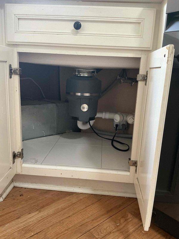 Completed plumbing estimate for kitchen fixture installation featuring an undermount sink with gold-finished faucet, matching soap dispenser, and garbage disposal system. Assessed existing white cabinetry configuration with proper drainage connections including white PVC piping and functional disposal unit with electrical hookup beneath sink area.