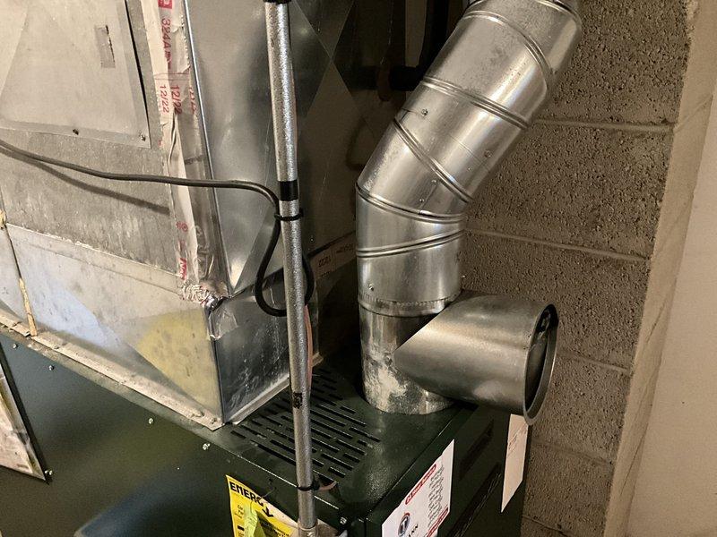 Completed comprehensive HVAC system assessment in residential basement utility area to provide replacement estimate. Evaluated existing dark green air handler/furnace unit with associated metallic ductwork configuration, including curved elbow sections routing along concrete block walls. Documented current system layout, ductwork condition, electrical connections, and mounting hardware to determine replacement specifications and installation requirements for updated heating and cooling equipment.