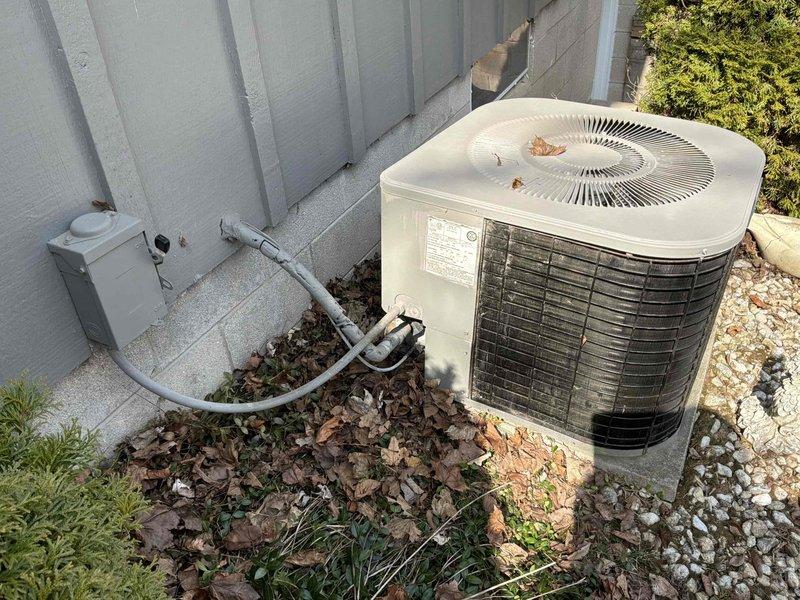 Completed comprehensive assessment of existing HVAC system for replacement estimate. Documented current outdoor condensing unit showing normal wear with debris accumulation on top cover and standard electrical disconnect configuration with PVC conduit routing from exterior wall. Inspected and photographed interior electrical panel in basement utility area, noting existing breaker configuration with one tripped breaker indicator and verifying available electrical capacity for new equipment installation.