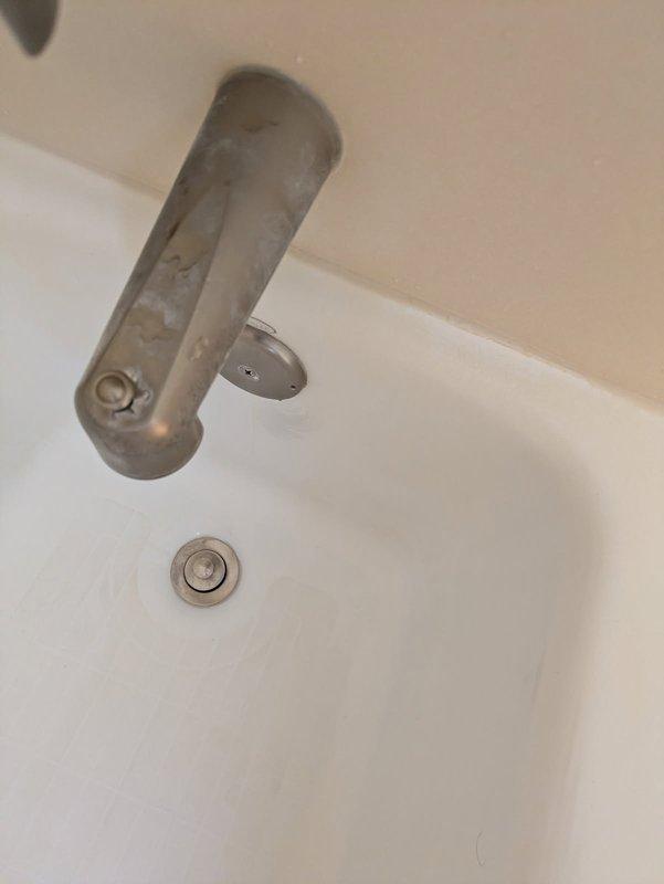 Responded to service call for malfunctioning bathtub diverter and tub spout assembly. Upon inspection, found the diverter handle detached and hanging improperly from mounting position, preventing proper operation of the shower/tub fixture. Removed the existing chrome diverter component and spout assembly from the ceiling-mounted configuration. Secured the diverter mechanism back into proper mounting position, ensuring flush installation against the wall surface. Tested the tub spout and diverter functionality to verify proper water flow direction between tub spout and showerhead. Additionally inspected the bathroom sink faucet and noted mineral deposits on the brushed metal finish but confirmed proper operational function of the wall-mounted single-handle fixture and popup drain assembly.