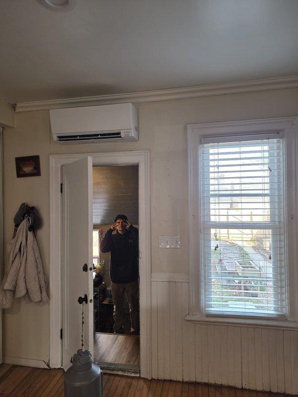 # HVAC Install - Mini Split

Completed installation of Mitsubishi Electric ductless mini-split system for residential heating and cooling. Mounted indoor wall unit above interior doorway in main living area with proper clearance and positioning for optimal air distribution. Installed outdoor condenser unit on wooden platform against exterior wall with secure mounting and level placement. Ran refrigerant lines and electrical connections through exterior wall penetration with appropriate sealing and weather protection. System tested for proper operation, refrigerant charge verified, and all components confirmed functional.