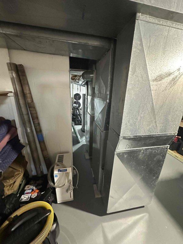 Completed HVAC system replacement in basement utility space, installing new air handler unit with updated ductwork connections. The existing equipment was removed and replaced with a modern silver-finished air handler, complete with foil insulation panels and properly configured supply and return duct connections to the ceiling plenum, ensuring efficient airflow distribution throughout the residence.