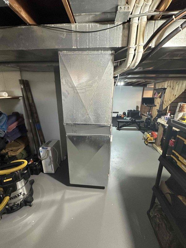 Completed HVAC system replacement in basement utility space, installing new air handler unit with updated ductwork connections. The existing equipment was removed and replaced with a modern silver-finished air handler, complete with foil insulation panels and properly configured supply and return duct connections to the ceiling plenum, ensuring efficient airflow distribution throughout the residence.