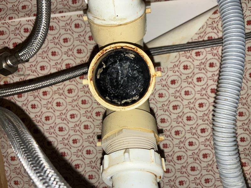 Responded to clogged drain call and performed diagnostic inspection of under-sink plumbing system. Upon investigation, discovered significant black buildup and debris accumulation inside brass T-fitting and connecting pipes, restricting water flow and causing drainage issues. Disassembled drain assembly including PVC connections and flexible supply lines. Thoroughly cleaned brass fitting interior, removing mineral deposits, corrosion, and accumulated sediment. Inspected all plumbing components for additional blockages or damage. Reassembled drain system with proper threading and sealing. Tested water flow and drainage to confirm full restoration of proper function. System now operating at normal capacity with no restrictions.