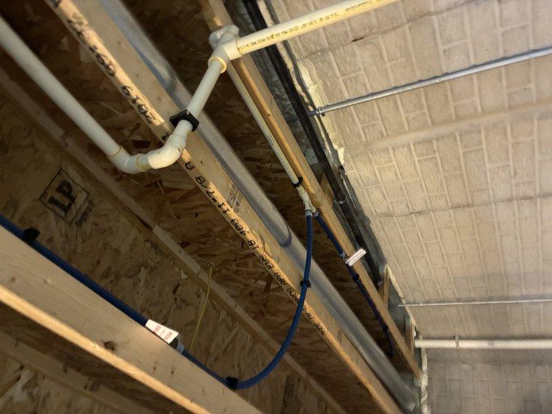 # Outdoor Spigot Installation and Plumbing Rough-In

Completed installation of outdoor spigot plumbing system during construction phase, routing new water supply lines through unfinished basement ceiling structure. Installed PVC and PEX piping with proper mounting brackets and clips along exposed floor joists, ensuring secure attachment and appropriate slope for drainage. Coordinated pipe routing with existing electrical conduit and HVAC systems to maintain proper clearances and building code compliance, preparing infrastructure for final connection to exterior hose bib fixture.