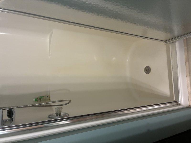 Completed installation of shower drain assembly and P-trap plumbing configuration in residential bathroom. Installed chrome drain cover with perforated grid pattern in fiberglass shower base and connected drainage system through subfloor using white PVC P-trap assembly with rubber coupling boots to existing dark drainpipe. Verified proper trap configuration for water seal and tested drainage flow to ensure no leaks at connection points.