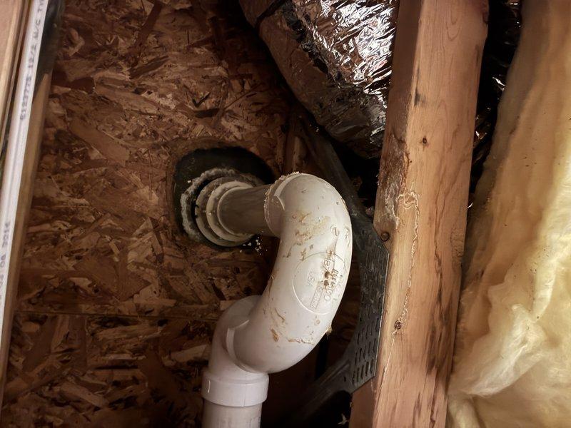 Completed installation of shower drain assembly and P-trap plumbing configuration in residential bathroom. Installed chrome drain cover with perforated grid pattern in fiberglass shower base and connected drainage system through subfloor using white PVC P-trap assembly with rubber coupling boots to existing dark drainpipe. Verified proper trap configuration for water seal and tested drainage flow to ensure no leaks at connection points.