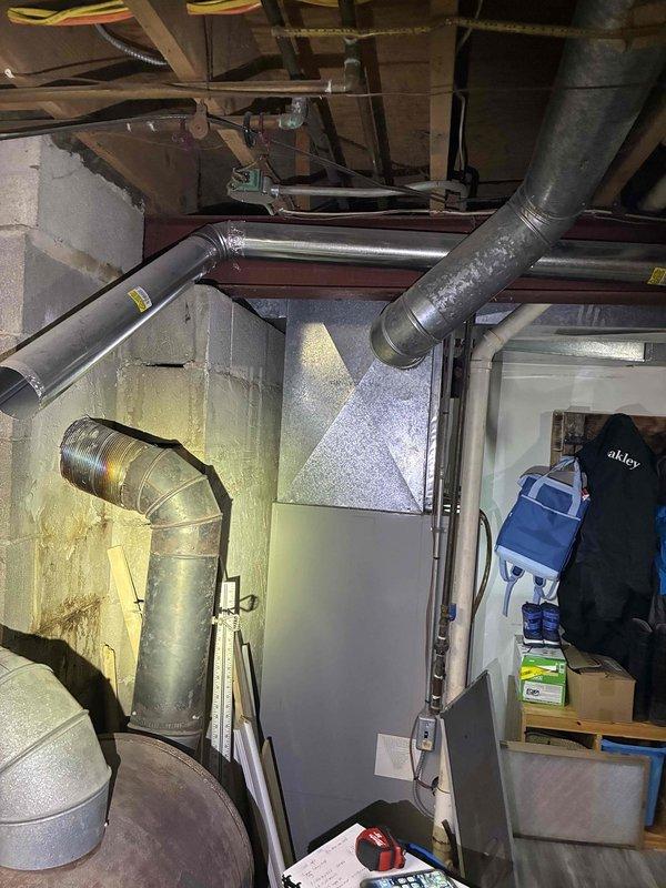 Completed comprehensive HVAC system assessment in basement utility area for equipment replacement estimate. Evaluated existing furnace unit, air handler, and associated ductwork configuration, documenting current system layout including rigid and flexible metal ducts, plenum connections, and structural mounting arrangements. Photographed equipment specifications, internal components with access panel open, and surrounding mechanical infrastructure to provide detailed replacement recommendations for aging heating system.