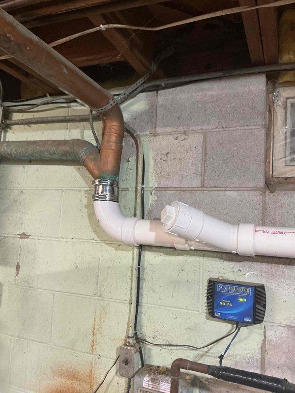 Completed plumbing estimate for sewer line system in basement utility area. Inspected existing drainage infrastructure including white PVC vertical and horizontal drain lines with coupling joints, copper pipe transitions with metal clamp connectors, and Sani-Panth sewage ejector pump system mounted on concrete block wall. Evaluated condition of plumbing connections, assessed pump operation and control unit functionality, and documented water staining on walls indicating potential drainage concerns requiring attention in comprehensive sewer line repair or replacement estimate.