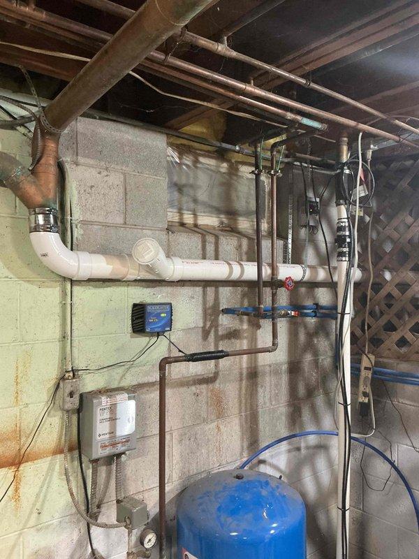 Completed plumbing estimate for sewer line system in basement utility area. Inspected existing drainage infrastructure including white PVC vertical and horizontal drain lines with coupling joints, copper pipe transitions with metal clamp connectors, and Sani-Panth sewage ejector pump system mounted on concrete block wall. Evaluated condition of plumbing connections, assessed pump operation and control unit functionality, and documented water staining on walls indicating potential drainage concerns requiring attention in comprehensive sewer line repair or replacement estimate.