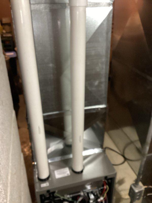 Completed installation of new HVAC furnace unit in utility space with proper venting and drainage configuration. Installed gray metal furnace cabinet with associated ductwork connections, secured white PVC condensate drain and vent piping with appropriate mounting brackets, and completed all electrical connections to manufacturer specifications. System tested and verified operational upon completion.