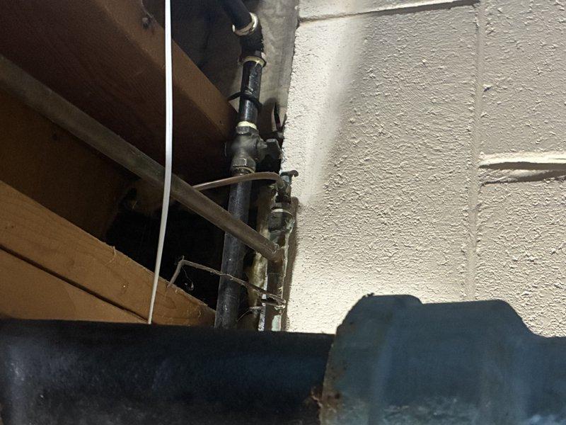 # Plumbing Inspection Report

Completed comprehensive plumbing inspection of drainage system and utility connections in crawl space area. Inspection revealed significant corrosion and green patina buildup on brass valve fitting connected to PVC P-trap assembly, indicating potential age-related deterioration requiring monitoring. Documented ceiling discoloration, rust staining around pipe connections, and overall condition of white PVC drainage piping, flexible corrugated metal hose, and black electrical cable routing through the space. Photographed exposed floor joists, structural framing, vertical black utility pipes with galvanized metal fittings, and textured wall surfaces to provide visual record of current system configuration and condition for future maintenance reference.