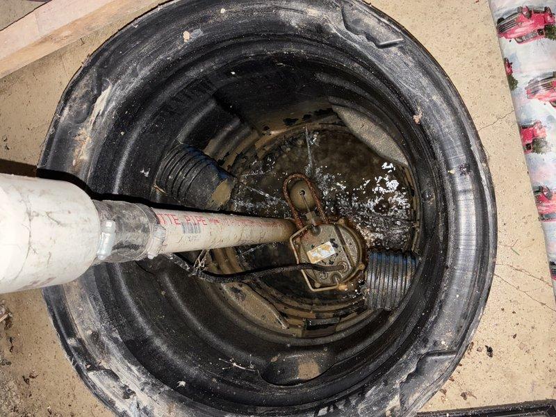 Performed inspection and assessment of existing sump pump system. Upon examination, found sump pump displaying significant corrosion, rust, and mineral deposit buildup on metal components, indicating extended service life and exposure to moisture. Pump was operational but showing clear signs of deterioration that could lead to future failure. Documented condition of circular ribbed plastic sump pit liner and verified proper water level within basin. Inspected white PVC discharge piping connection at pump assembly and traced exterior discharge line. Exterior inspection revealed black corrugated flexible drainage hose routing water away from foundation to appropriate drainage area at lawn perimeter. Verified discharge system was properly directing water away from structure to prevent foundation issues. Photographed all system components for maintenance records. Recommended monitoring pump performance and considering replacement due to advanced corrosion to prevent potential emergency fai