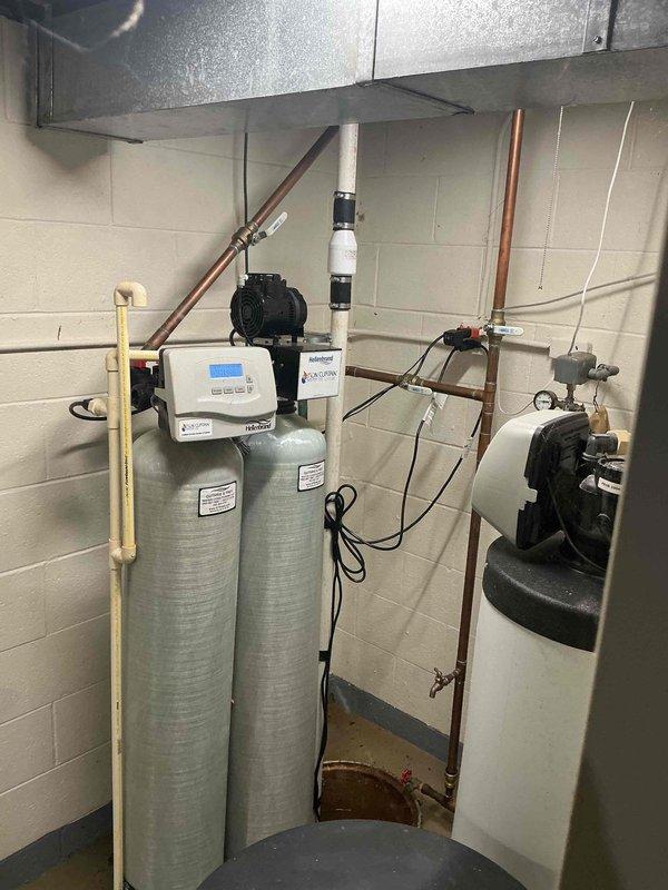 Performed inspection and maintenance of residential sump pump system located in basement utility area. Documented existing sump pump installation within concrete basin, noting rust staining on basin walls and water presence indicating active use. Verified pump operation and assessed discharge piping configuration, including white PVC discharge line. Photographed complete system setup including connection points to ensure proper documentation of equipment condition and plumbing connections for service records.