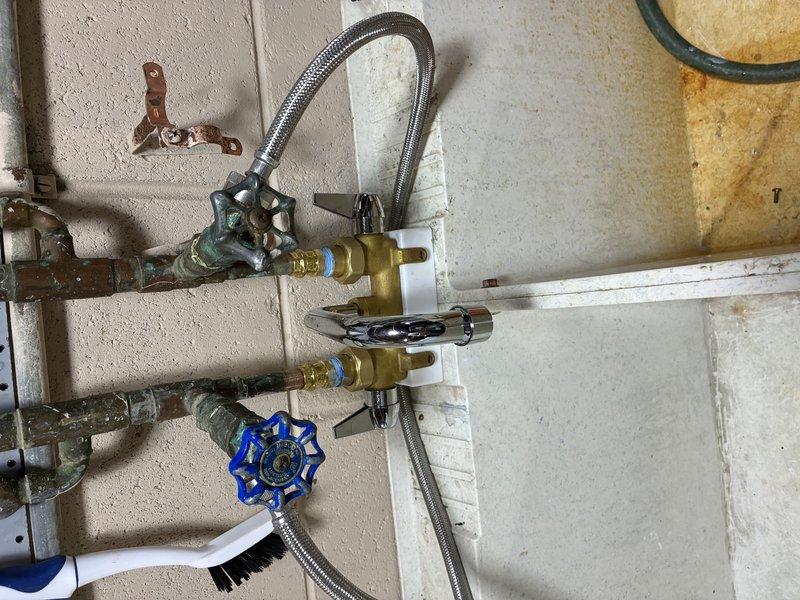 Completed water service installation connecting supply lines to water heater. Installed shut-off valves on copper supply lines with flexible braided stainless steel connectors, utilizing brass fittings with rubber washers to ensure proper sealing and prevent leaks at connection points.