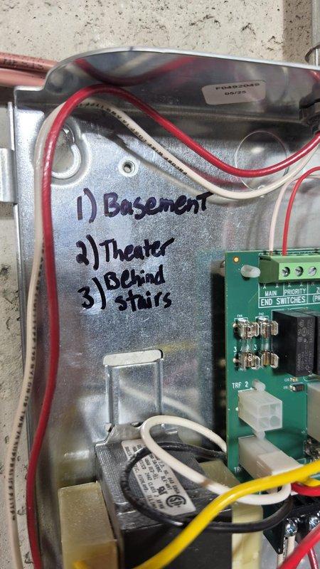 Completed installation of NTI tankless boiler system with multi-zone radiant heating distribution in basement location. Mounted main boiler unit to concrete wall with proper clearances and connected extensive copper manifold piping system for zone control. Installed two zone control panels, expansion tank, and integrated yellow-handled gas shutoff valves throughout the piping network. Secured all copper supply and return lines with black mounting brackets at appropriate intervals for code compliance. Ran white PVC exhaust venting vertically for proper combustion air and flue gas management. Wired electrical control panel with zone identification for basement, theater, and behind-stairs areas, including main battery backup and switching components. Mounted gray transformer and control board within electrical enclosure for system operation. Installed condensate management equipment at floor level. Tested all zones for proper operation, verified gas connections for leaks, confirmed electr