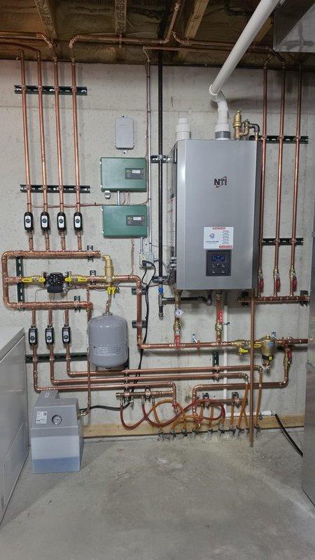 Completed installation of NTI tankless boiler system with multi-zone radiant heating distribution in basement location. Mounted main boiler unit to concrete wall with proper clearances and connected extensive copper manifold piping system for zone control. Installed two zone control panels, expansion tank, and integrated yellow-handled gas shutoff valves throughout the piping network. Secured all copper supply and return lines with black mounting brackets at appropriate intervals for code compliance. Ran white PVC exhaust venting vertically for proper combustion air and flue gas management. Wired electrical control panel with zone identification for basement, theater, and behind-stairs areas, including main battery backup and switching components. Mounted gray transformer and control board within electrical enclosure for system operation. Installed condensate management equipment at floor level. Tested all zones for proper operation, verified gas connections for leaks, confirmed electr