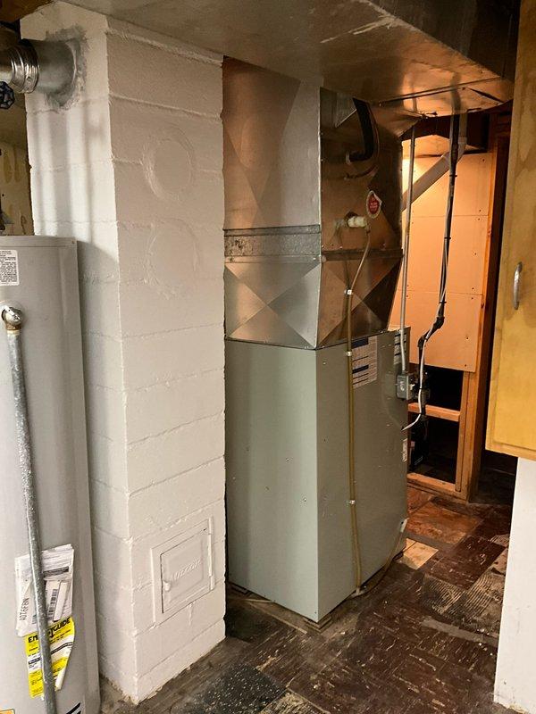 Completed residential HVAC system replacement in basement utility area, installing new furnace unit with proper PVC venting configuration and sheet metal plenum integration. Existing equipment was removed and replaced with modern high-efficiency system, including proper ductwork connections and exhaust/intake venting routed through dual white PVC pipes to ensure safe combustion air management and code-compliant installation.