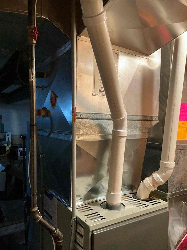 Completed residential HVAC system replacement in basement utility area, installing new furnace unit with proper PVC venting configuration and sheet metal plenum integration. Existing equipment was removed and replaced with modern high-efficiency system, including proper ductwork connections and exhaust/intake venting routed through dual white PVC pipes to ensure safe combustion air management and code-compliant installation.