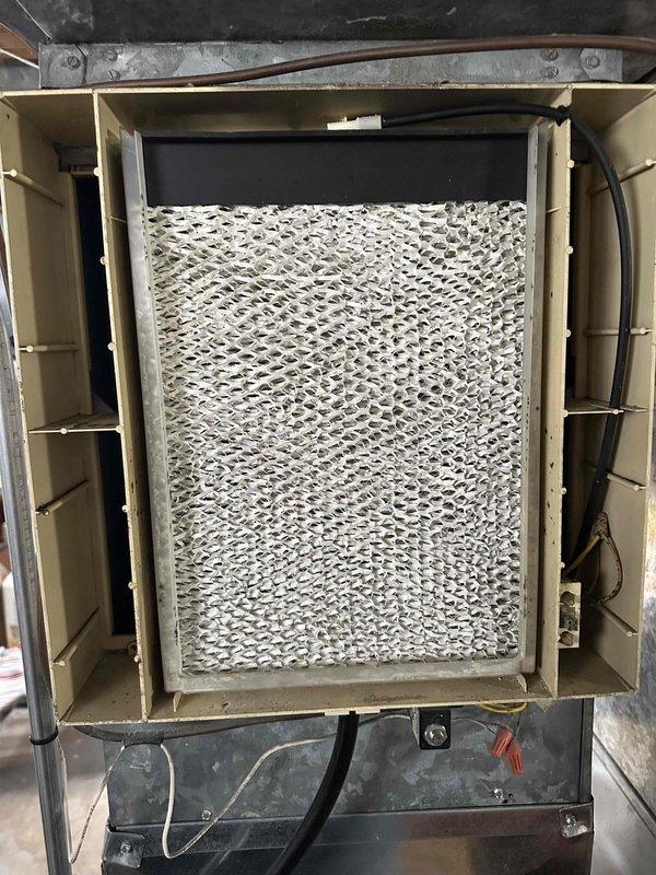 Performed comprehensive HVAC system assessment in residential basement mechanical room for equipment replacement estimate. Evaluated existing furnace unit with connected gray metal ductwork system and associated ventilation infrastructure. Inspected air handler filter compartment, noting filter condition with visible dust accumulation and normal wear patterns. Documented current system configuration including PVC condensate drainage piping, electrical connections, and ductwork routing through ceiling joists. Assessed installation space constraints and existing mechanical room layout to determine optimal replacement equipment specifications and installation requirements.