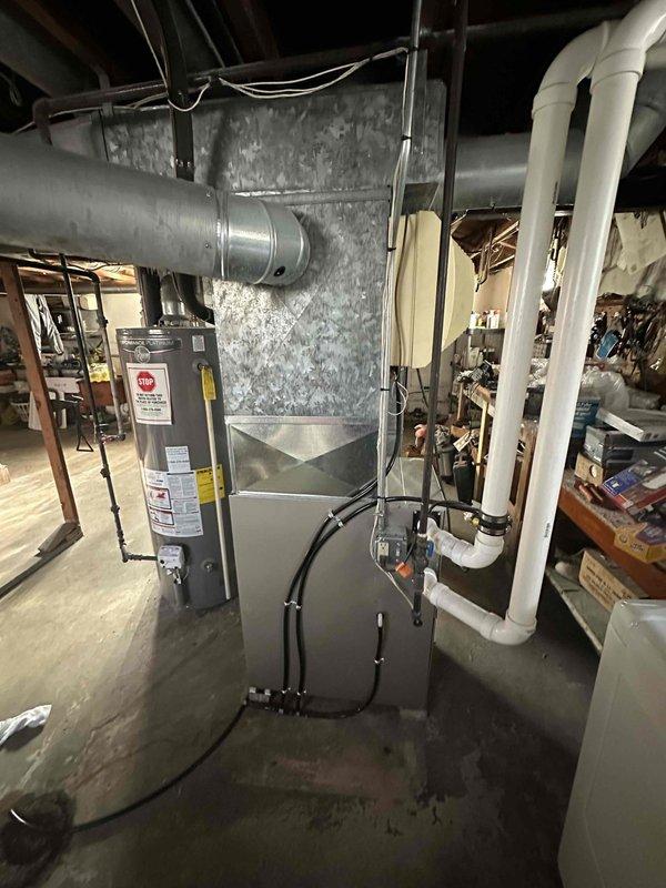 Performed comprehensive HVAC system assessment in residential basement mechanical room for equipment replacement estimate. Evaluated existing furnace unit with connected gray metal ductwork system and associated ventilation infrastructure. Inspected air handler filter compartment, noting filter condition with visible dust accumulation and normal wear patterns. Documented current system configuration including PVC condensate drainage piping, electrical connections, and ductwork routing through ceiling joists. Assessed installation space constraints and existing mechanical room layout to determine optimal replacement equipment specifications and installation requirements.