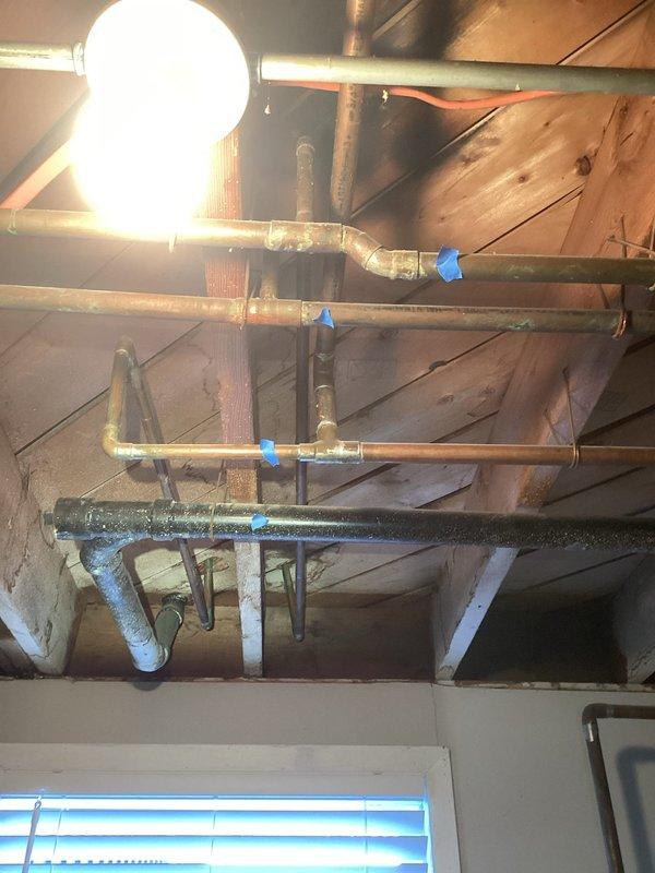 Performed comprehensive inspection of boiler system and associated piping infrastructure in attic space. Documented existing copper supply lines and PVC condensate drainage system, noting multiple connection points marked for reference. Evaluated condition of horizontal pipe runs supported by wooden joists, including sections with reflective insulation wrapping. Assessed aging metal piping showing surface oxidation and verified structural support integrity throughout the installation. Inspected complex PVC joint configurations and confirmed proper drainage routing from boiler system.